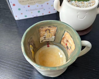 Può includere: Una tazza in ceramica con esterno verde salvia e interno giallo chiaro. Le pareti interne presentano illustrazioni dipinte a mano di opere d'arte incorniciate. Dietro la tazza c'è una scatola bianca con pois colorati e il testo kilnsolo.com.
