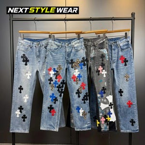 Puede incluir: Cuatro pares de pantalones vaqueros de mezclilla colgados en un perchero de metal negro. Los pantalones presentan varios parches en forma de cruz en colores como rojo, blanco, azul, negro y estampado de leopardo. El texto NEXT STYLE WEAR es visible.