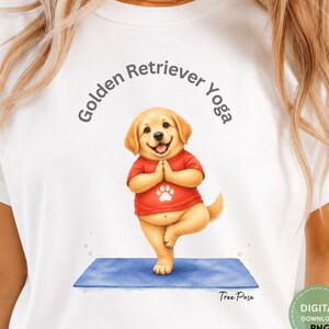 May include: A white t-shirt featuring a graphic of a golden retriever puppy wearing a red shirt with a white paw print, performing a yoga tree pose on a blue mat. The text "Golden Retriever Yoga" is arched above, and "Tree Pose" is below.