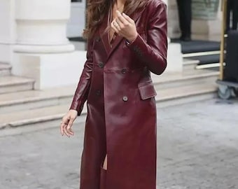 May include: A long, double-breasted burgundy leather coat featuring a notched lapel, structured shoulders, long sleeves with buttoned cuffs, and two flap pockets at the waist. The coat is paired with matching burgundy leather knee-high boots.