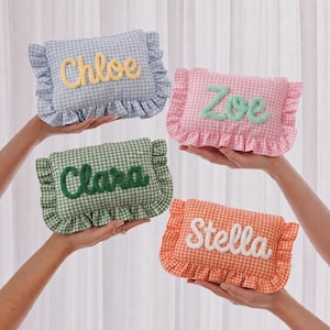 May include: Four rectangular fabric pouches with ruffled edges and a gingham pattern in light blue, pink, green, and orange. Each pouch features a name embroidered in raised script lettering: Chloe in yellow, Zoe in mint green, Clara in dark green, and Stella in white.
