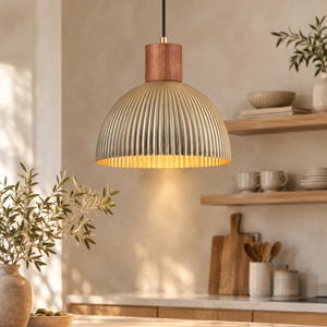 May include: A dome-shaped pendant light featuring a ribbed, metallic silver exterior and a warm gold-toned interior. The fixture is suspended by a black cord and includes a cylindrical wooden accent piece at the top connection point.