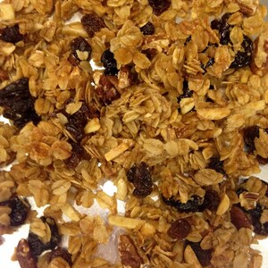 May include: A close-up of a bowl of granola with oats, almonds, pecans, and raisins. The granola is golden brown and appears to be homemade.