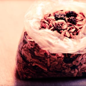 May include: A clear plastic bag filled with granola, a mixture of oats, nuts, and dried fruit. The granola is a light brown colour and the dried fruit is a dark red colour.