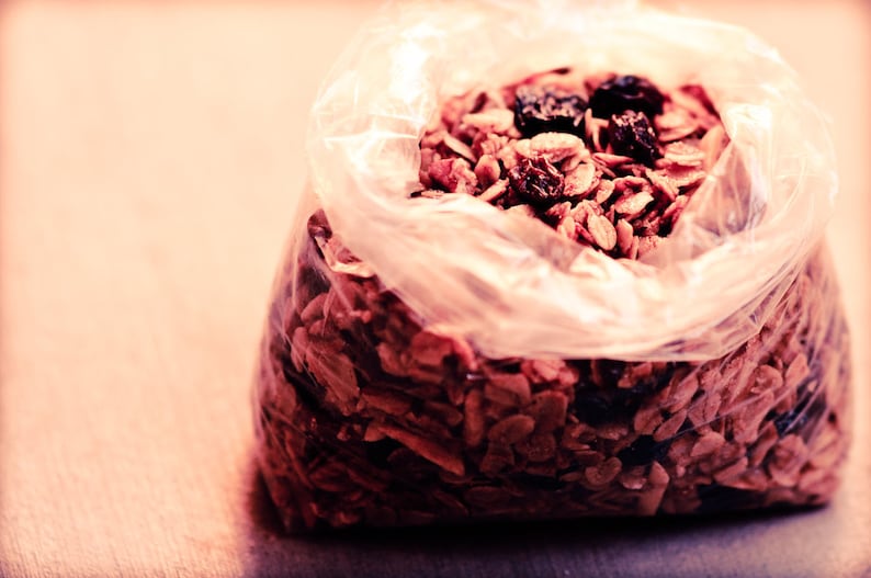 May include: A clear plastic bag filled with granola, a mixture of oats, nuts, and dried fruit. The granola is a light brown colour and the dried fruit is a dark red colour.