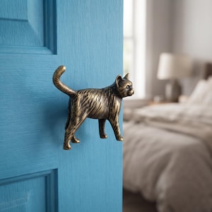 May include: A metallic, bronze-toned cat-shaped door handle mounted on a bright blue door. The cat is depicted in a standing profile position with its tail curved upward, featuring detailed textured fur markings across its entire body surface.