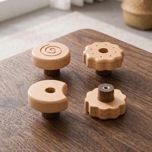 Peut inclure: Quatre boutons de meuble en bois clair aux formes distinctes. L'un est circulaire avec une spirale gravée, un autre est un cercle festonné avec un trou central, un est en forme de croissant avec un trou, et le dernier est un cercle festonné.