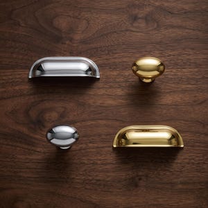 May include: A collection of four cabinet hardware pieces consisting of two polished chrome and two polished brass items. The set includes two semi-circular cup pulls and two smooth, rounded knobs, all featuring a reflective, high-gloss metallic finish.