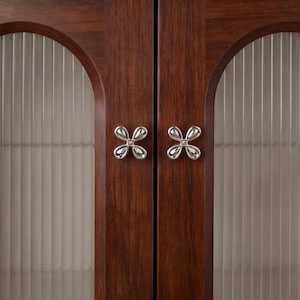 May include: A pair of dark brown wooden cabinet doors featuring arched glass panels with vertical fluting. Each door is fitted with a polished silver-toned metal knob shaped like a four-petaled flower, centered on the vertical wooden frame.