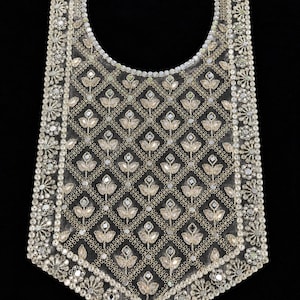 May include: A sheer fabric neckline applique featuring intricate silver embroidery and small circular mirrors arranged in a repeating diamond pattern with floral motifs, finished with a dense border of metallic floral and mirror embellishments.