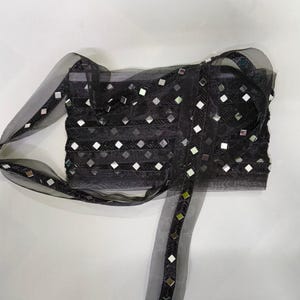May include: A black sheer organza ribbon featuring a repeating pattern of small square mirrors and black beaded chevron embroidery. The decorative trim has a translucent texture and is arranged in multiple overlapping horizontal layers.