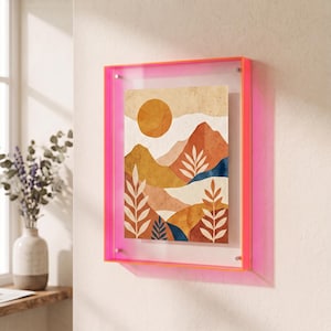 May include: A rectangular wall art piece featuring a stylized landscape with a large orange sun, layered mountain ranges in shades of tan, brown, and blue, and white leaf illustrations, all encased in a vibrant neon pink acrylic frame.