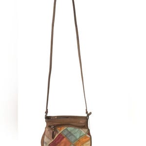 May include: A small brown leather crossbody bag featuring a patchwork design on the front panel. The patchwork consists of various muted colors including red, orange, yellow, green, and blue squares. It has a long thin strap and a zippered top.