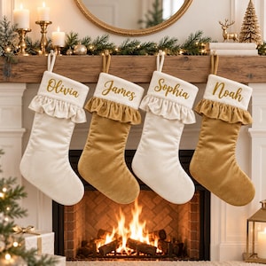 Può includere: Quattro calze di Natale appese in fila, che si alternano tra tessuto di velluto color crema e oro. Ogni calza presenta un risvolto con volant e un nome personalizzato in scrittura glitterata dorata: Olivia, James, Sophia e Noah.