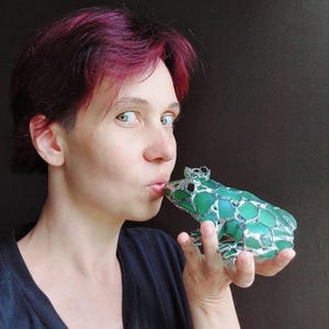 Peut inclure: Une figurine de grenouille décorative construite à partir de multiples morceaux de verre de mer vert maintenus ensemble par des lignes de soudure en métal argenté. La grenouille a un aspect texturé en mosaïque avec des nuances de verre vert.
