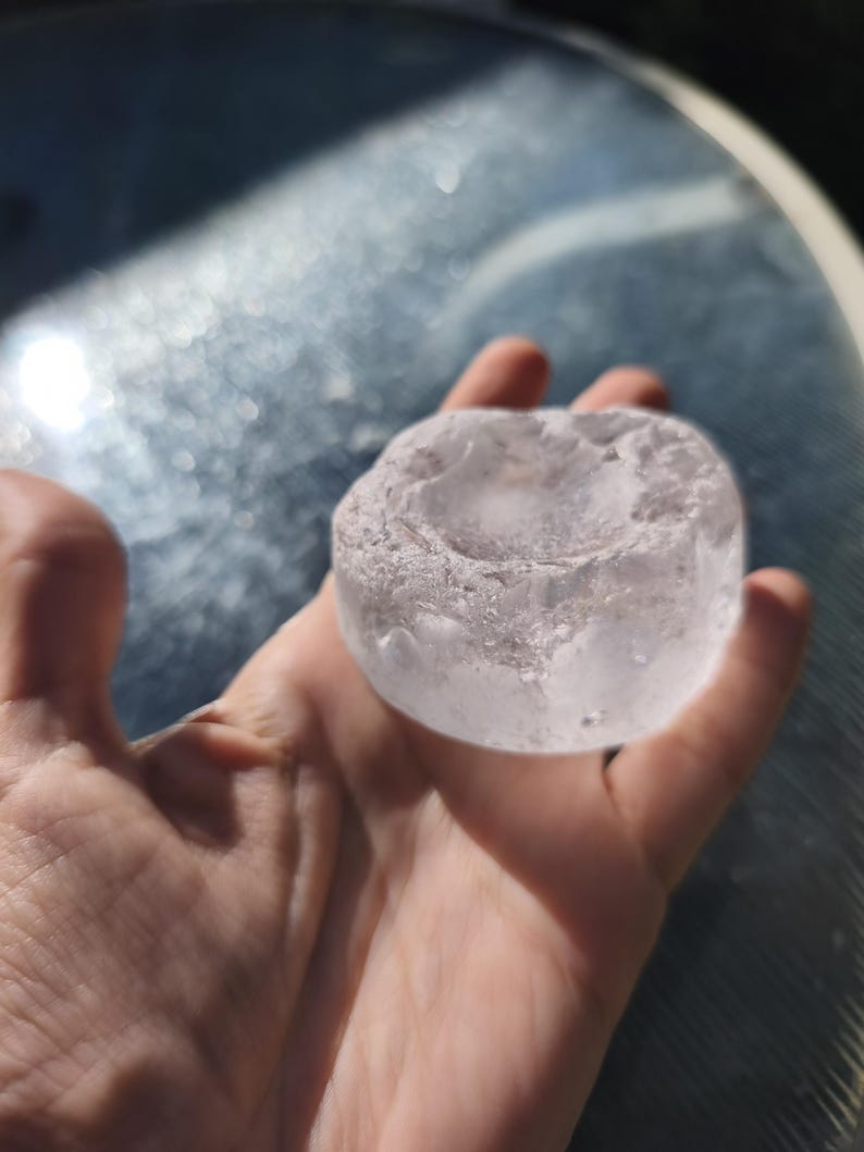 May include: A circular, translucent, and colorless object with a rough, uneven texture and a shallow, concave depression in the center. The item appears to be made of a solid, clear material with a slightly frosted or crystalline surface finish.