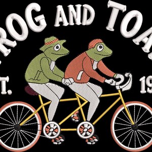 May include: An embroidered design on a black background featuring two frogs riding a yellow tandem bicycle. The frog in front wears a green hat and jacket, while the other wears a red jacket. Text reads FROG AND TOAD EST. 1942 in white letters.