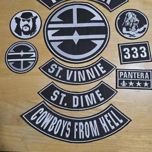 May include: A collection of black and white embroidered patches featuring the band Pantera. The set includes a large circular logo, three curved rocker patches with the text Pantera, St. Vinnie, St. Dime, and Cowboys From Hell, plus smaller circular and rectangular patches with portraits, the number 333, and stars.