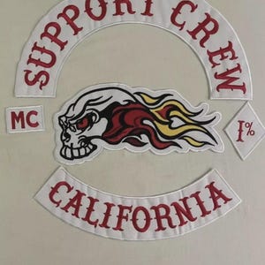 May include: A set of embroidered patches featuring a white arched top rocker with red text reading SUPPORT CREW, a bottom rocker with red text reading CALIFORNIA, a small MC patch, a diamond 1% patch, and a central skull with red and yellow flames.