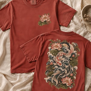 Może przedstawiać: Ceglastoczerwony t-shirt z krótkim rękawem, ozdobiony małą grafiką kwiatu lotosu na lewej piersi oraz dużym, szczegółowym nadrukiem na plecach przedstawiającym dwie ryby koi pływające wśród kwiatów lotosu, liści lilii wodnych i fal.