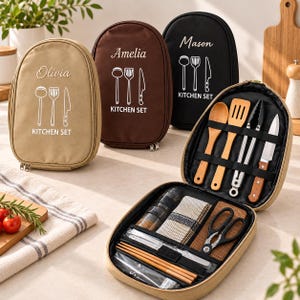 Peut inclure: Trois étuis à ustensiles de cuisine ovales à fermeture éclair en beige, marron et noir, personnalisés avec un nom et un graphique blanc de louche, spatule et couteau. Un étui beige est ouvert, révélant des ustensiles en bois, des pinces et des ciseaux.