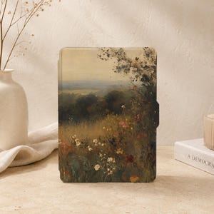 May include: A rectangular e-reader case featuring a printed landscape painting of a rolling meadow with wildflowers in the foreground, dark green trees in the mid-ground, and a soft, hazy sky in the distance, rendered in muted earth tones.