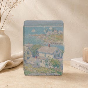 以下が含まれることがあります： 海岸の風景を描いた印象派風の絵画がプリントされた長方形の電子書籍リーダーケース。赤い煙突のある白い家々が草の生い茂る丘に立ち、帆船が浮かぶ青い湾を見下ろす様子が柔らかな色調で表現されています。