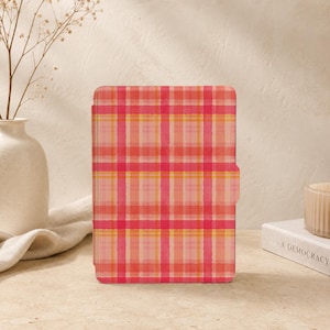 Peut inclure: Un étui rectangulaire pour liseuse électronique arborant un motif à carreaux vibrant dans des tons de rose, corail et jaune. La couverture présente une surface lisse et plate avec une petite languette sur le côté droit, affichant une grille régulière.