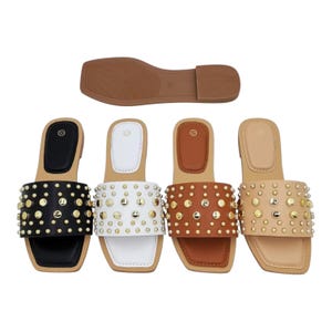 May include: Four flat slide sandals with square toes, each featuring a wide strap adorned with gold-tone metal studs. The sandals are available in black, white, brown, and beige, with a separate brown sole shown above the four pairs of sandals.