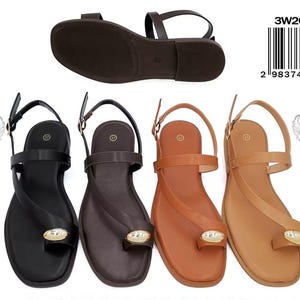 May include: Four flat sandals in black, dark brown, tan, and light brown, each featuring a toe loop, an ankle strap with a buckle, and a central oval metallic embellishment. A single sandal sole is shown above, with a barcode labeled 3W26-306B.