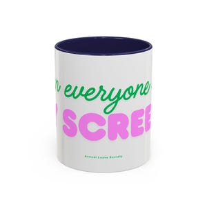 Op de afbeelding: Een witte keramische mok met een donkerblauwe binnenrand. De buitenkant bevat groene cursieve tekst "on everyone" boven grote roze blokletters "SCREEN" en de kleine groene tekst "Annual Leave Society" aan de onderzijde.