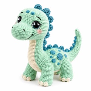Può includere: Un peluche a forma di dinosauro lavorato all'uncinetto in verde menta con pancia color crema, spine dorsali blu scuro e macchie circolari blu abbinate sul fianco. La creatura ha grandi occhi neri, un sorriso ricamato e artigli color crema.