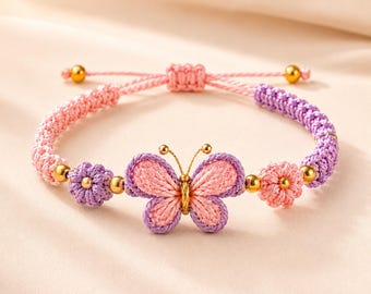 May include: A woven cord bracelet featuring a central butterfly charm with pink and purple thread, flanked by two small flower-shaped beads. The band consists of alternating pink and purple braided cord sections accented with small gold-toned metal beads.