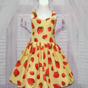 May include: A yellow and white gingham dress with a strawberry print. The dress has thin straps and a full skirt.