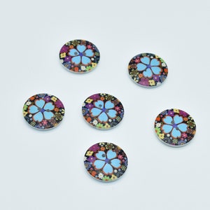 May include: Six round wooden buttons with a blue flower design on a black background. The flowers are surrounded by smaller multi-colored flowers.