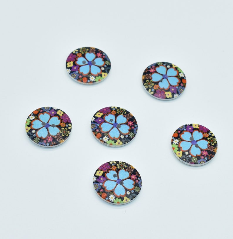 May include: Six round wooden buttons with a blue flower design on a black background. The flowers are surrounded by smaller multi-colored flowers.