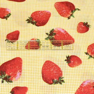 May include: Yellow fabric with a white checkered pattern and a repeating pattern of red strawberries.