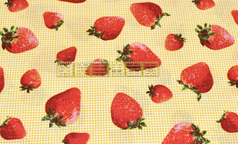 May include: Yellow fabric with a white checkered pattern and a repeating pattern of red strawberries.