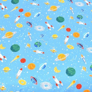 Könnte beinhalten: Ein blauer Stoff mit einem sich wiederholenden Muster aus Planeten, Sternen, Kometen und Raketen. Die Planeten sind in verschiedenen Farben, darunter Gelb, Orange, Grün und Blau. Die Raketen sind rot und weiß.