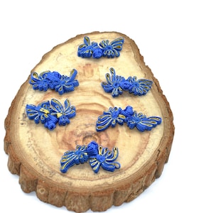 May include: A collection of blue and gold floral-shaped embellishments arranged on a rustic wooden slice. The embellishments feature intricate detailing and a contrasting gold trim, creating a decorative element.