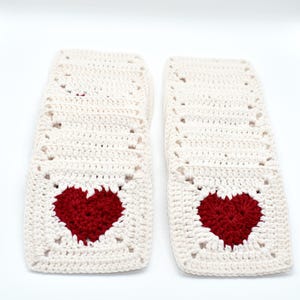 May include: Cream-coloured crocheted squares with a red heart in the centre. The squares are stacked in two separate piles. The yarn has a textured appearance. The hearts are a deep, rich red colour.
