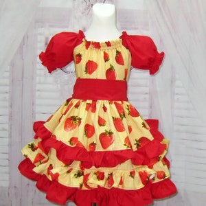 May include: A yellow and red dress with a strawberry print and multiple layers of ruffles. The dress has short sleeves and a red sash.