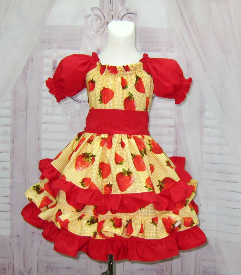 May include: A yellow and red dress with a strawberry print and multiple layers of ruffles. The dress has short sleeves and a red sash.