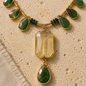May include: A necklace featuring a gold-tone chain with small green cylindrical beads and faceted green teardrop-shaped stones. A large rectangular faceted yellow stone hangs from the center, topped by a smaller green teardrop-shaped stone.