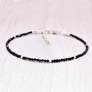 Puede incluir: Una pulsera delicada con pequeñas cuentas negras facetadas dispuestas en un patrón circular, acentuada con diminutos espaciadores metálicos plateados y un cierre de mosquetón plateado con una cadena de extensión ajustable.