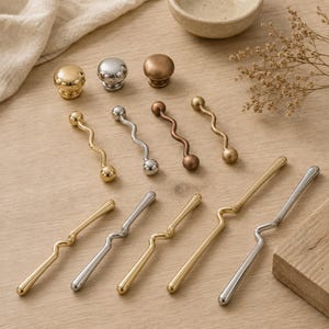 May include: A collection of metal hardware including three round knobs in gold, silver, and bronze finishes, four short wavy drawer pulls in matching metallic tones, and five long, slender, offset handles in gold and silver finishes.