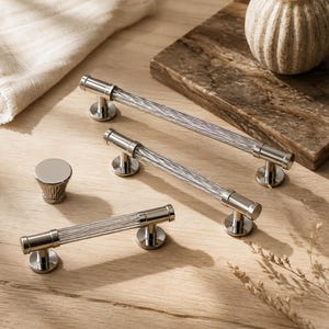 May include: A collection of cabinet hardware including three silver-toned metal handles with clear, ribbed glass center bars and one matching silver-toned metal knob with a smooth, flat top and a textured, tapered base design.