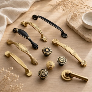 May include: A collection of cabinet hardware including various drawer pulls and knobs in brushed gold, antique brass, and matte black finishes. The set features ornate floral detailing, smooth curved handles, and circular knobs with intricate patterns.