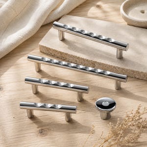 May include: A collection of four silver-toned metal cabinet pulls and one matching round cabinet knob. Each pull features a cylindrical bar design with a series of concave circular indentations along the top surface and two cylindrical mounting posts.