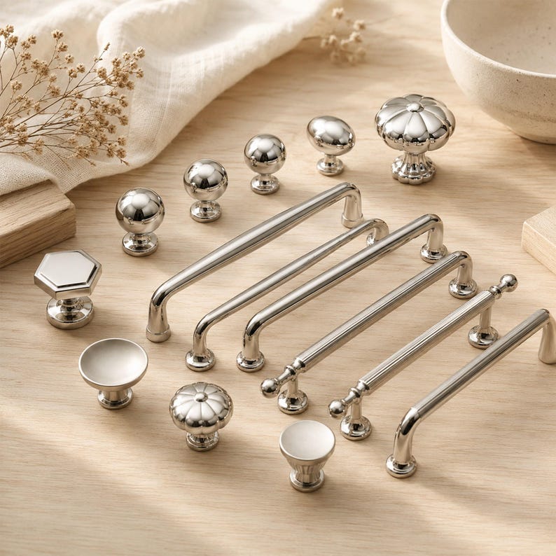 May include: A collection of silver-toned metal cabinet hardware including various drawer pulls and knobs. The set features smooth spherical knobs, a hexagonal knob, fluted round knobs, and several elongated bar handles with polished finishes.